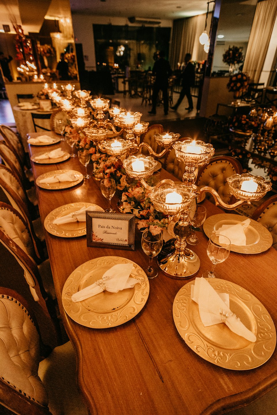Elegante tavolo da pranzo apparecchiato con piatti dorati e candelabri accesi.